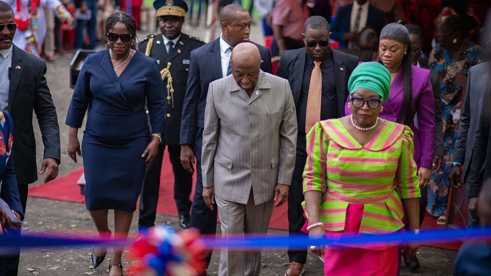 Officials walking along a red carpet behind a ceremonial ribbon at an outdoor commissioning event.